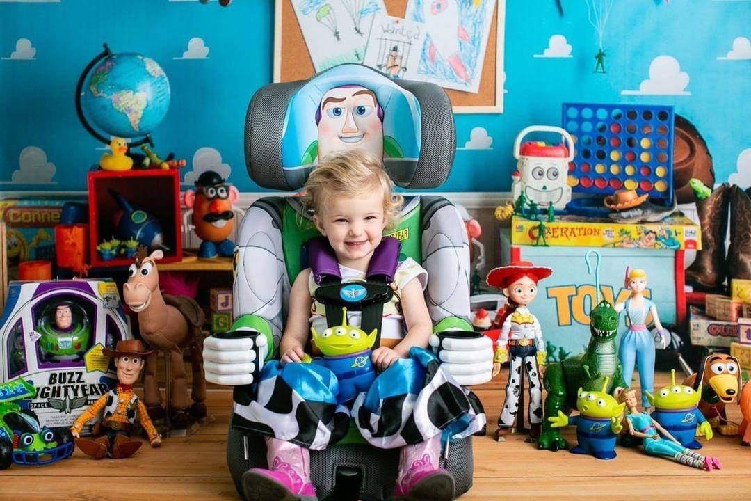 Baby sitting in a Buzz Lightyear car seat surrounded by Toy Story toys