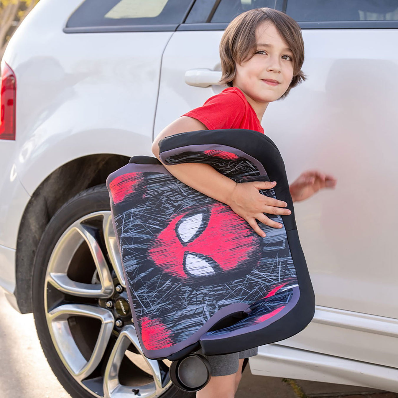 Young boy carrying his own Spiderman booster car seat